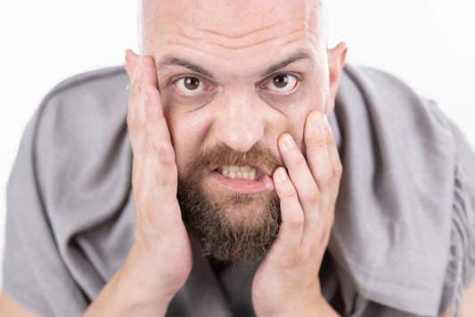 Homme portant la main à sa mâchoire tendue, un signe fréquent de tension liée à la posture respiratoire